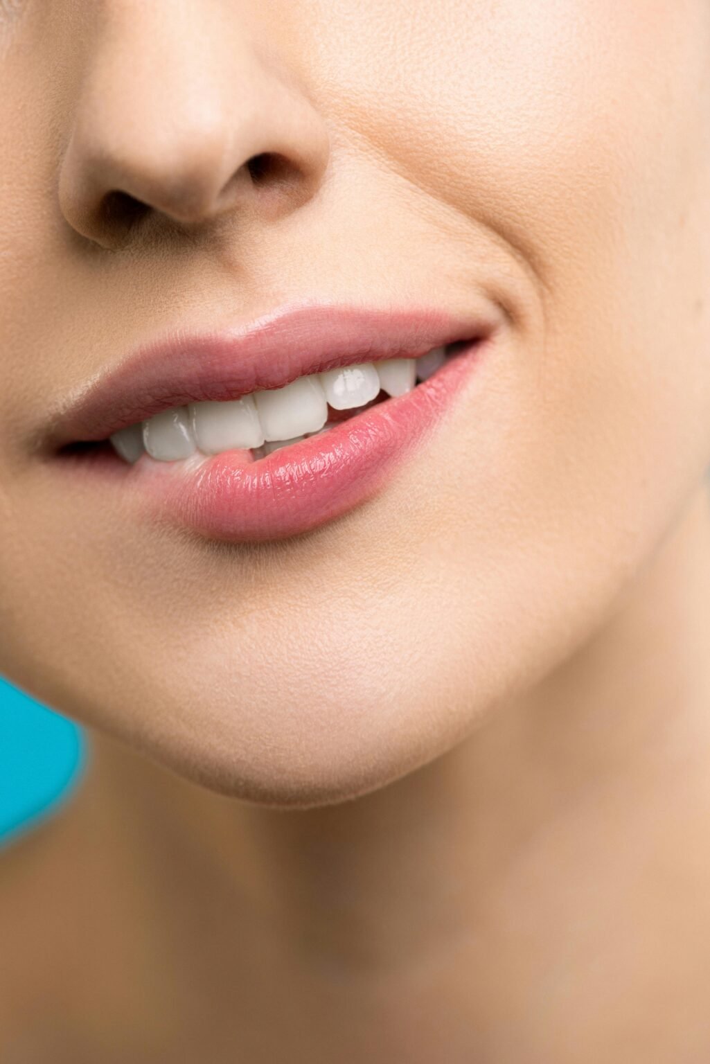 A detailed close-up of a woman's smile highlighting her lips and teeth with pink lipstick.