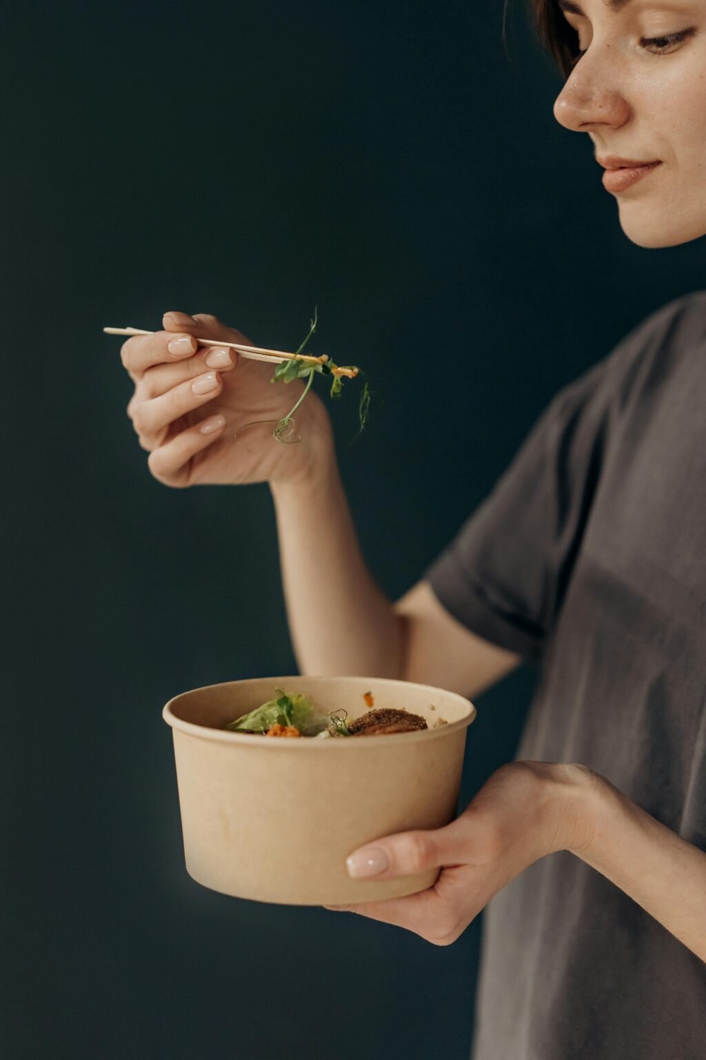 Woman enjoying a nutritious salad bowl with fresh vegetables using chopsticks.