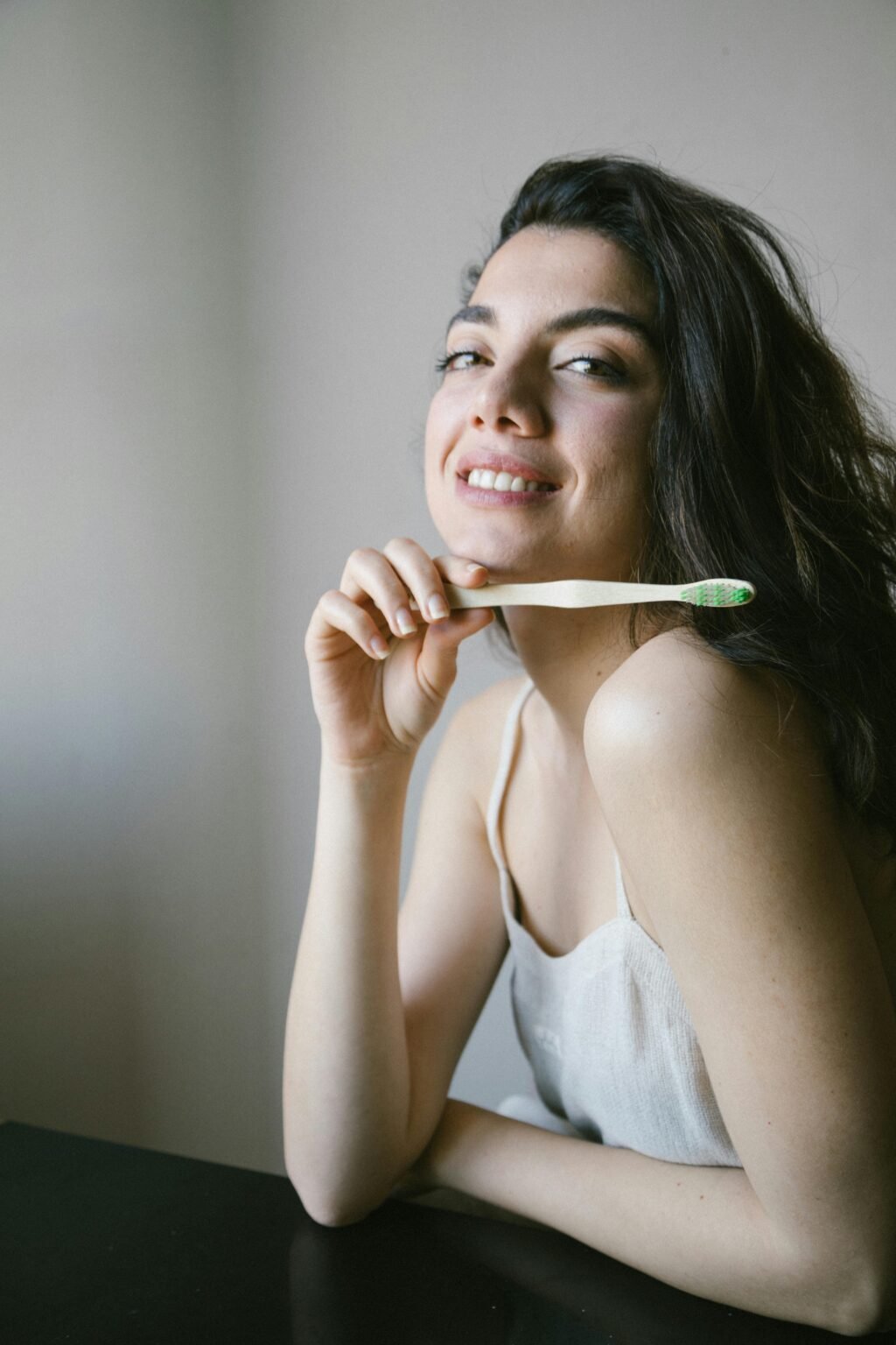 Woman smiling holding an eco-friendly toothbrush, promoting dental hygiene and sustainability.